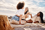 Three young mixed race female friends hanging out and having wine at the beach. Hispanic women having a glass on wine outdoors