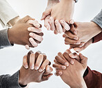 Below view of people holding hands in circle shape. A group of people putting their hands together while standing in a huddle inside against a clear grey background. Anything is possible with teamwork
