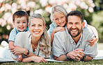Young happy caucasian family relaxing and lying on grass together in a park. Loving parents spending time with their son and daughter in nature. Joyful siblings hugging their mom and dad outside