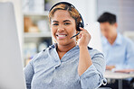 Portrait of one happy young mixed race female call centre telemarketing agent talking on a headset while working on a computer in an office. Confident and friendly african american businesswoman consultant operating helpdesk for customer service support