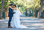 Young bride and groom enjoying romantic moments outside on a beautiful summer day in nature. Full length shot of newlywed couple touching foreheads while standing close