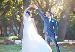 Joyful bride and groom sharing a dance in nature. Groom spins his bride during romantic dance at park on their wedding day