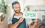 One young hispanic man hanging up an "open" sign in at a window on display in a cafe or store. Happy mixed race guy excited to open his shop and welcome customers