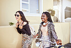 Two happy hipster female friends laughing and having fun in city street. Positive carefree women enjoying a walk down the street with a bicycle