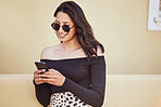 Happy young mixed race girl with sunglasses using her smartphone while standing on sidewalk. Stylish woman sending a text or chatting on social media while on city street