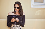 Happy young woman with sunglasses using earphones to listen to music on smartphone or watch funny video online. Pretty mixed race girl using mobile app while standing on sidewalk