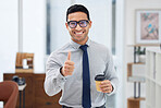 Portrait of a young happy mixed race businessman holding a cup of coffee and showing a thumbs up in an office at work. Male hispanic businessperson smiling while showing support with a thumbs up