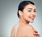 Portrait of a beautiful mixed race woman touching smooth soft skin in a studio. Hispanic model with healthy natural glowing skin looking confident against grey copyspace while doing routine skincare