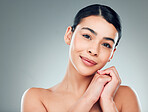 Portrait of a beautiful mixed race woman with smooth soft skin in a studio. Hispanic model with healthy natural glowing skin looking confident against grey copyspace while doing routine skincare