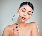 A beautiful mixed race woman posing with a magnifying glass. Young hispanic obsessed with targeting acne and wrinkles against a grey copyspace background