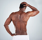 Rear view of one African American fitness model posing topless in a towel and looking muscular. Black male athlete rubbing his head while isolated on grey copyspace in a studio