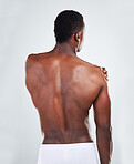One unknown muscular fitness model experiencing shoulder pain from an injury while exercising. Black topless athlete holding his arm in pain while isolated on grey copyspace in a studio