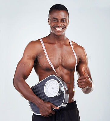 Buy stock photo Portrait of a smiling African American fitness model posing topless with a scale and measuring tape. Happy black male athlete isolated on grey copyspace showing the thumbs up to a healthy diet