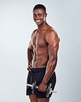 Portrait of a smiling African American fitness model posing topless while exercising with dumbbells .Happy black male athlete isolated on grey copyspace while weightlifting in a studio