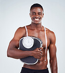 Portrait of a smiling African American fitness model posing topless with a scale and measuring tape. Happy black male athlete isolated on grey copyspace and looking happy with his diet