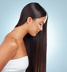 A hispanic brunette woman with long lush beautiful hair posing and looking serious against a grey studio background. Mixed race female standing showing her beautiful healthy hair