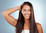 Portrait of a hispanic brunette woman with long lush beautiful hair smiling and posing against a grey studio background. Mixed race female standing showing her beautiful healthy hair