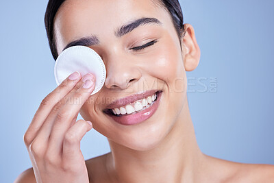 Buy stock photo A beautiful smiling mixed race woman using a cotton pad to remove makeup during a selfcare grooming routine. Hispanic woman applying cleanser to her face against blue copyspace background