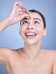 A beautiful happy mixed race young woman with glowing skin posing against blue copyspace background while tweezing her eyebrows. Hispanic model using a tweezer for hair removal