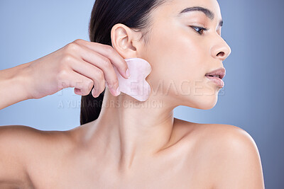 Buy stock photo A beautiful mixed race woman using a rose quartz gua sha to reduce wrinkles and promote cell renewal. Young hispanic woman using anti ageing tool against blue copyspace background