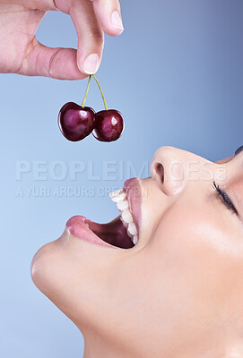 Buy stock photo A happy smiling mixed race woman eating a cherry. Hispanic model promoting the skin benefits of a healthy diet against a blue copyspace background