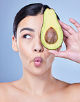 A beautiful young mixed race woman holding a sliced avocado. Hispanic model with glowing skin holding a fruit against a blue copyspace background