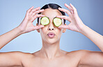 A beautiful mixed race woman holding cucumber slice. Hispanic model using cucumber sooth her eyes against a blue copyspace background