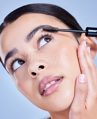 Buy stock photo Closeup of a beautiful young mixed race woman with glowing skin posing against blue copyspace background. Hispanic woman with natural looking eyelash extensions applying mascara