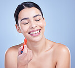 A beautiful young mixed race woman with glowing skin posing against blue copyspace background. Hispanic woman applying lipstick in a studio