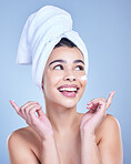 A beautiful smiling mixed race woman applying cream to her cheek. Hispanic model with towel wrapped hair using lotion against a blue copyspace background