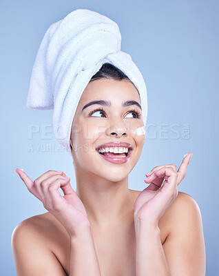 Buy stock photo A beautiful smiling mixed race woman applying cream to her cheek. Hispanic model with towel wrapped hair using lotion against a blue copyspace background
