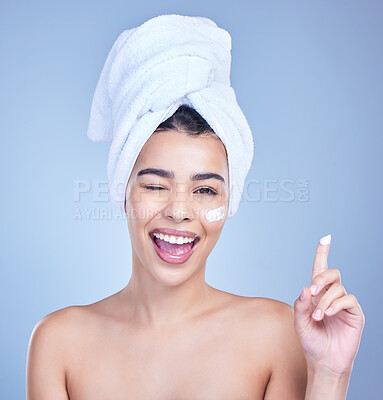 Buy stock photo Studio Portrait of a beautiful smiling mixed race woman applying cream to her face. Hispanic model with glowing skin and wet hair against a blue copyspace background