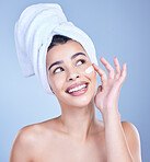 A beautiful smiling happy mixed race woman applying cream to her face. Hispanic model with glowing skin against a blue copyspace background