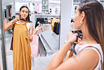 Mixed race woman looking at her reflection in a store mirror. Young female happy while fitting on clothes at a boutique. Smiling and spending money on a fashion sale. Woman holding bags while shopping