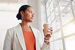 Young mixed race businesswoman looking out of a window while drinking a coffee alone in an office at work. Confident hispanic businessperson looking out of a window drinking a coffee on a break while standing at work