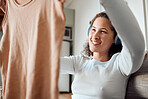 Woman listening to music in headphones. Young woman looking at fresh, cleaned laundry. Happy woman holding washed top. Young woman enjoying music and housework chores. Woman cleaning her clothing