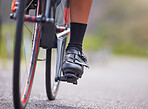 Closeup of the feet of one young woman exercising outside in the forest. Healthy and sporty female athlete with her feet on pedals out for a cycle. Endurance and cardio during a workout in the woods