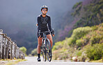 One athletic young woman cycling outside. Sporty fit female wearing helmet and glasses while riding a bike on a road along the mountain for exercise. Endurance and cardio during a workout and training