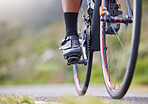 Closeup of one woman cycling outside. Sporty fit female athlete with her feet on bicycle pedals while riding a bike on a road for exercise. Endurance and cardio during a workout and training