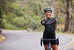 A happy athletic mixed race young woman wearing a helmet showing thumbs up outside .Healthy and sporty female athlete out for a ride on her bicycle in the woods