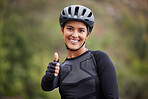 A happy athletic mixed race young woman wearing a helmet showing thumbs up outside .Healthy and sporty female athlete out for a ride on her bicycle in the woods