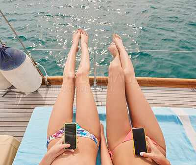 Buy stock photo Two friends sunbathing on boat during holiday cruise together using cellphones to send text messages. Two women lying on boat using smartphones and sunbathing in bikinis