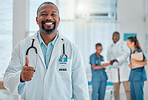 Mature african american male doctor showing a thumbs up while working at a hospital with colleagues. Expert medical professional smiling while making a hand gesture in support at work at a clinic