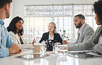 Group of five diverse businesspeople talking in a meeting together at work. Business professionals talking and planning in an office. Young african american businesswoman discussing an idea with colleagues at a table