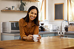 Portrait of a young happy beautiful mixed race woman enjoying a cup of coffee alone at home. One cheerful hispanic female in her 20s drinking a cup of tea in the kitchen at home