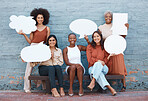 Group of five young happy cheerful businesswomen standing and sitting on a bench against a wall outside in the city and holding speech bubbles. Businesspeople smiling holding contact details boards outdoors