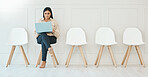 Full body indian businesswoman sitting alone and using a laptop to browse the internet while waiting for an interview. Creative candidate searching online for vacancies. Staying connected and online