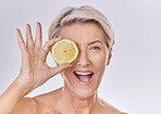 Portrait of a  happy smiling caucasian woman holding a lemon. Mature model promoting the skin benefits of a healthy diet against a purple  copyspace background