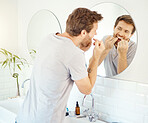 One handsome man flossing his teeth in a bathroom at home. Caucasian male using floss to prevent cavities while looking in a mirror in his apartment