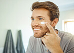 One handsome man applying cream or moisturiser to his face in a bathroom at home. Caucasian male using a lotion or sunscreen in his apartment